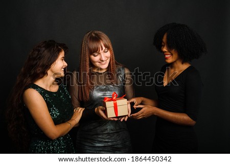 Image of beautiful three young woman rejoicing while standing with present box isolated over black background during christmas celebration