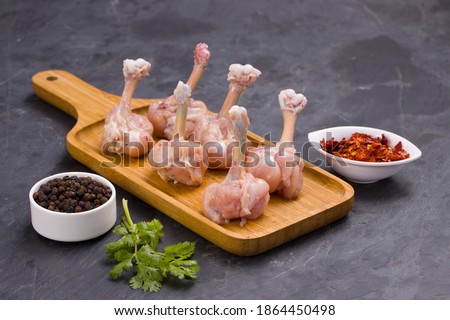 Raw chicken lollipop,six pieces of chicken lollipop arranged on a serving board with black pepper,chilli flakes and coriander leaf with grey textured background Royalty-Free Stock Photo #1864450498