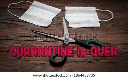 QUARANTINE IS OVER text. End of the Covid 19 pandemic. Scissors cut the medical mask. Wooden background