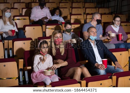 Group of people of different ages and nationalities wearing protective face masks to prevent viral infections absorbedly watching movie in cinema