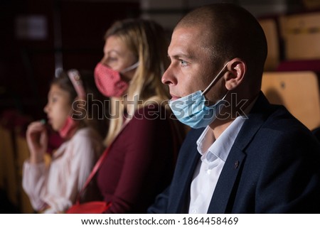 Portrait of man wearing medical face mask sitting in cinema with his family, watching movie. Entertainment concept in coronavirus pandemic