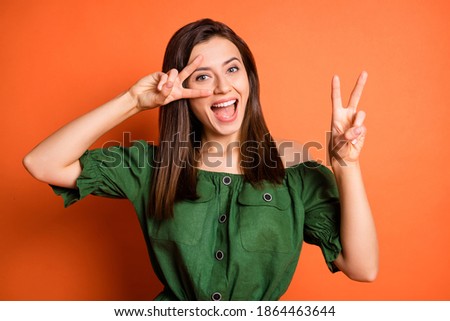 Portrait of optimistic cute woman show v-sign wear dark shirt isolated on orange color background