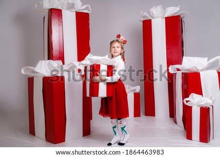 happy funny child girl in Christmas costume with big red gifts on background.