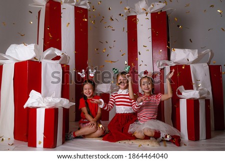 funny little girs lfriends in Christmas costumes against the background of big red presents. idea and concept of a happy holiday, new year, friendship and childhood.
