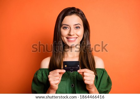 Photo of optimistic sweet girl hold card wear dark shirt isolated on orange color background