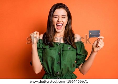 Photo of funny lucky lady wear green off-shoulders blouse rising fist holding bank card isolate orange color background