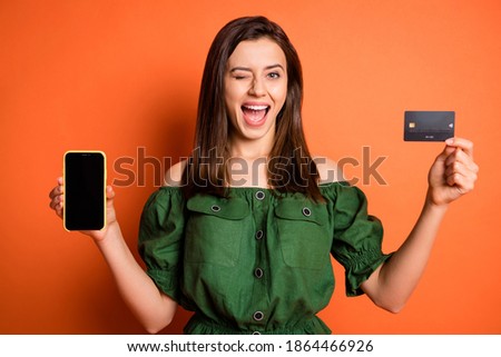 Photo of funny lady wear green off-shoulders blouse holding bank card modern device winking isolated orange color background