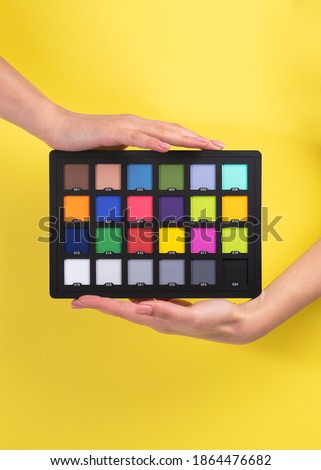 Color checkerboard passport. Professional Photography Chip chart for color calibration. Girl hands hold color check pallet card isolated on yellow background