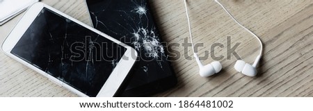 Top view of earphones with smashed smartphone on wooden background, banner
