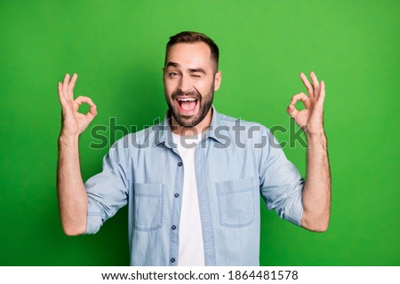 Portrait of cool guy show okey sign blink wear blue shirt isolated on vibrant green color background