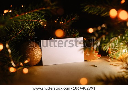 Blank business card with christmas tree branches and golden garland lights. New year celebration concept banner. Gift certificate. Side view. Cozy frame decoration. Invitation to an event or party. Royalty-Free Stock Photo #1864482991