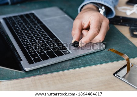 Cropped view of repairman holding broken key of laptop keyboard at workplace on blurred background