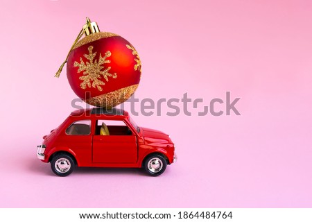 Minsk, Belarus, 23 november 2020. Concept christmas background. Red retro toy car delivering Christmas or New Year gifts, ball, on pink background