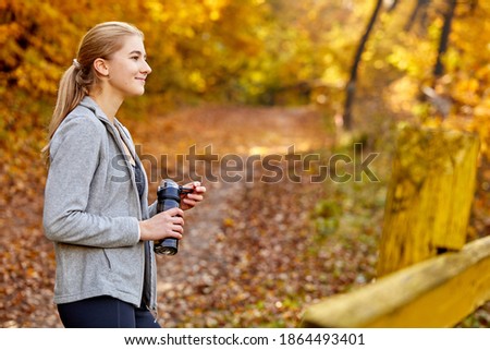 caucasian sporty woman with bottle of water outdoors, young female resting after training.exhausted joggewoman resting after jogging on the autumnal forest hill, side view