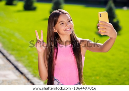 Photo of small schoolgirl hold telephone shoot selfie show v-sign shiny smile wear pink top urban city outside