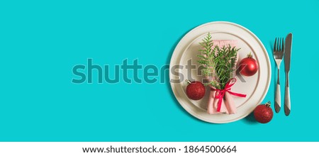 Website banner with served plate and cutlery for celebration of Christmas and New Year. On plate is a napkin with Christmas tree branch, red balls. Flatlay banner on bright blue background. Top view.