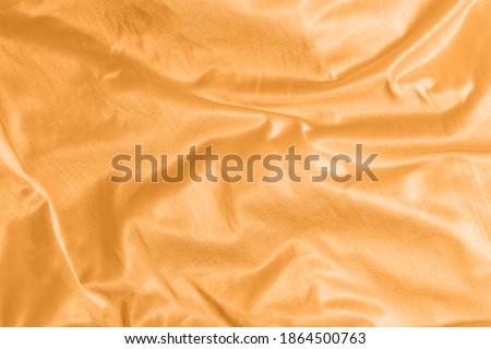Shiny satin silk fabric with folds background texture textile. Tinted in 2021 color orange marigold.