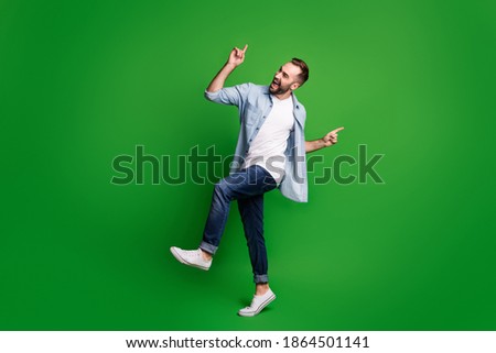 Full size profile photo of optimistic guy dancing wear blue shirt jeans footwear isolated on green color background