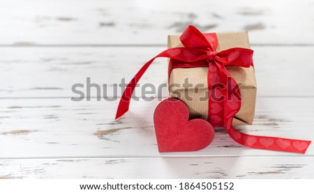 Gift box with a red ribbon and heart shape on white wooden Valentines background. 