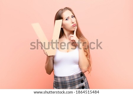 yound blonde woman confused, doubtful, thinking, holding the letter V of the alphabet to form a word or a sentence.