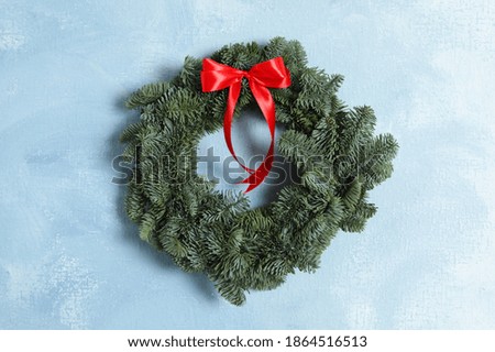 Christmas wreath made of fir tree branches with red ribbon on light blue textured background