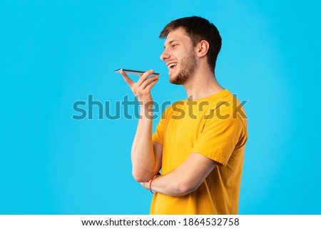 Phone Call, Mobile Communication And Voice Assistant Concept. Smiling Bearded Man Talking On Smartphone Using Loudspeaker Mode, Guy Standing Isolated Over Blue Studio Background, Copy Space