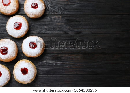 Hanukkah doughnuts with jelly and sugar powder on black wooden table, flat lay. Space for text