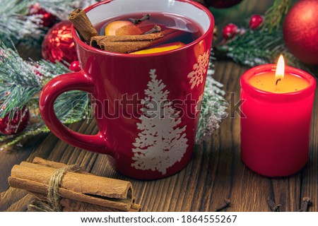 view of a cup with a Christmas candle, hot mulled wine, with spices and fruits on a wooden rustic table background with fir branches. Traditional hot drink for Christmas.