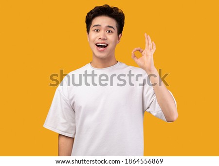 I'm Fine. Portrait of happy excited asian guy doing approval ok gesture with fingers, smiling, showing that he is okay, isolated over orange studio background. Confident positive teen is cool