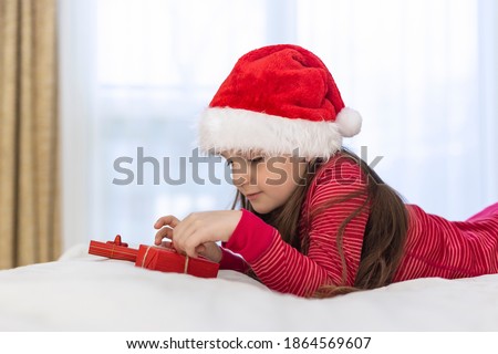 little girl brunette in red santa hat unpacking christmas gifts .