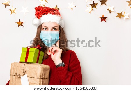 Young pensive girl in a red sweater with a medical mask holds wrapped gifts for the New Year and Christmas in her hands. White background, banner, place for text or congratulations