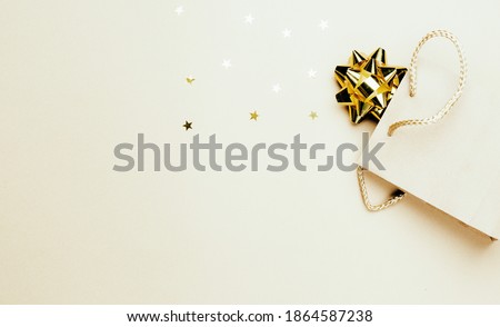 Paper bag with New Year's gifts on beige and champagne color background flat lay,