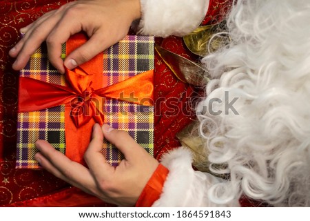 man dressed as Santa Claus is tying a bow on a red ribbon on a checkered box. beard. Christmas. New Year. gift wrapping. concept. minimalistic. vintage. preparation for shipment. horizontal. close up.