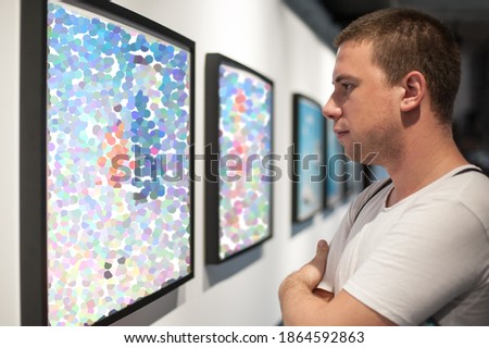 Young man in modern art exhibition gallery hall contemplating artwork. Abstract painting