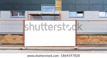 large white banner with place for template at grid fence against building with narrow windows at summer sunlight