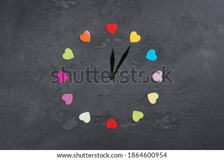 Enjoy every moment, love, Valentine concept. Clock with colorful hearts hours on gray concrete background. Flat lay, top view, copy space