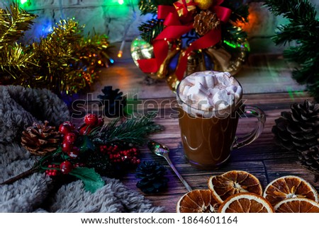 a glass Cup of marshmallow coffee is on the table, along with a spoon, cones, dried orange slices and a sprig of spruce, a soft gray scarf and new moon toys