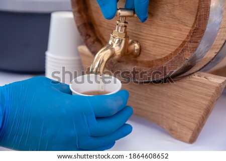 Hands with gloves. A man pours a drink from an oak barrel.