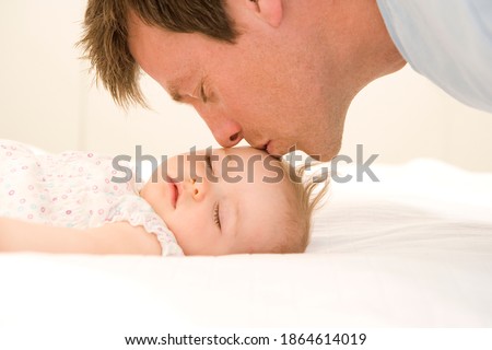 Horizontal close up a loving father kissing his baby girl's forehead as the baby is asleep