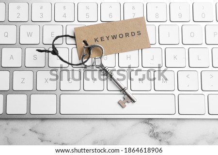Keyboard, vintage key and tag with word KEYWORDS on white marble table, top view Royalty-Free Stock Photo #1864618906