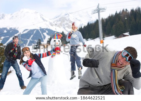 Horizontal shot of a two young couples having a snow fight in a snow covered field on a bright, sunny day next to a snowman