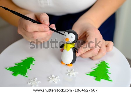 Handy baker making penguin figure of fondant. On the white pad are visible already made snowflakes and Christmas trees.