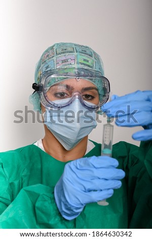 Nurse looks at the needle, equipped with gloves, cap, goggles and mask