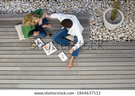 Horizontal overhead shot of a couple with the man feeding sushi with chopsticks to the woman on a patio with copy space.