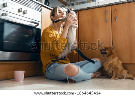 Shot of beautiful young woman playing with her cute lovely animals sitting on the floor in the kitchen at home.
