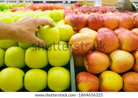 Horizontal close up shot of a woman's hand picking up a green apple from a pile at the supermarket.