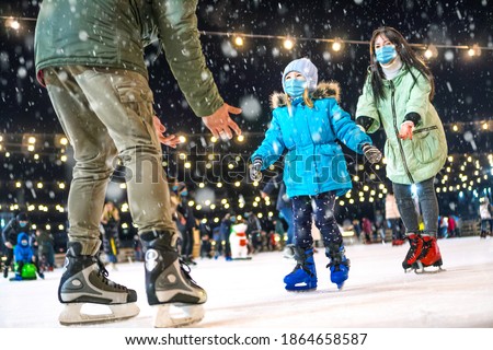 Skating rink. Family wearing the medical face masks on the ice rink. Prevention of coronavirus and other infectious diseases during the winter holidays concept. Mom and dad teach daughter to skate.