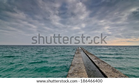 Road to Freedom - alone concrete pier with clear ocean and stormy clouds