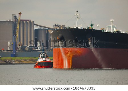 Large crude oil tanker ship pumping out ballast water when coming into port in Rotterdam, tug boat pushing the side Royalty-Free Stock Photo #1864673035