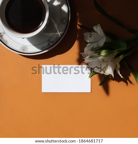 Flat lay of branding identity business name card on a ginger background with a white flower, a cup of coffee, light and shadow. Flat lay, top view. Work, business concept. Home office desk workspace.